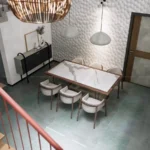 A modern dining hall with a marble-top table, six upholstered chairs, textured white accent wall, and pendant lights