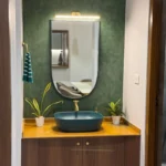 modern wash base vwith green ceramic basin wood countertop,indoor plants,and a round mirror in interior designers in malappuram
